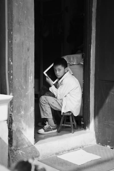 student artwork by Joey Zheng entitled old town memories. a black and white photograph of a boy sitting on a stool in a doorway