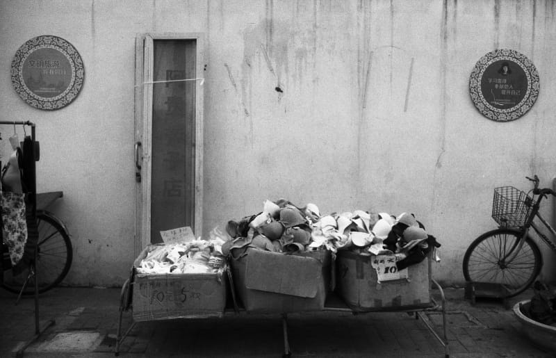 student artwork by Joey Zheng untitled. a black-and-white photograph of three boxes in an ally full of bras for sale